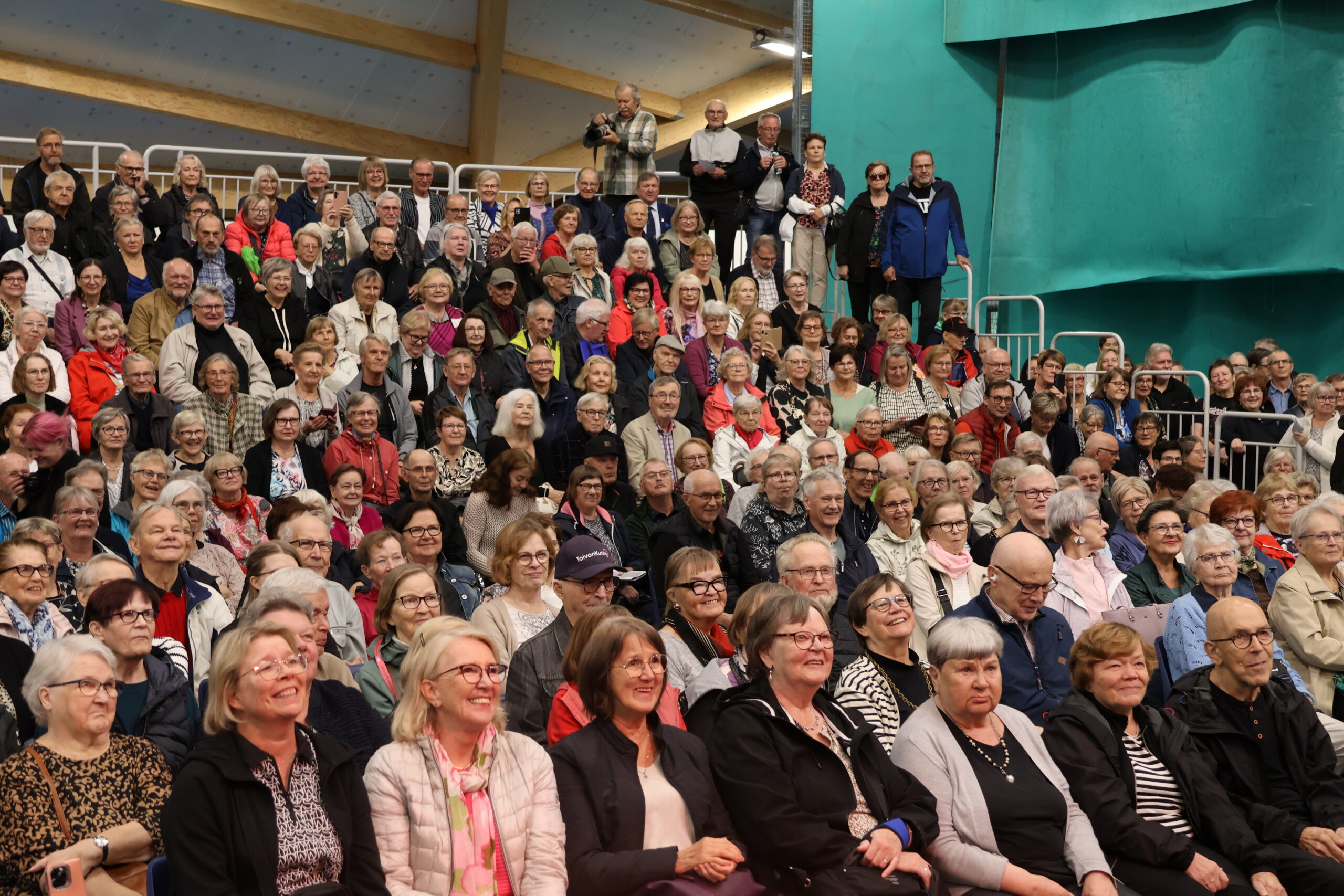 Iloinen yleisö katsoo messuohjelmaa Rakentajamessuilla, kaikki eivät mahdu istumaan