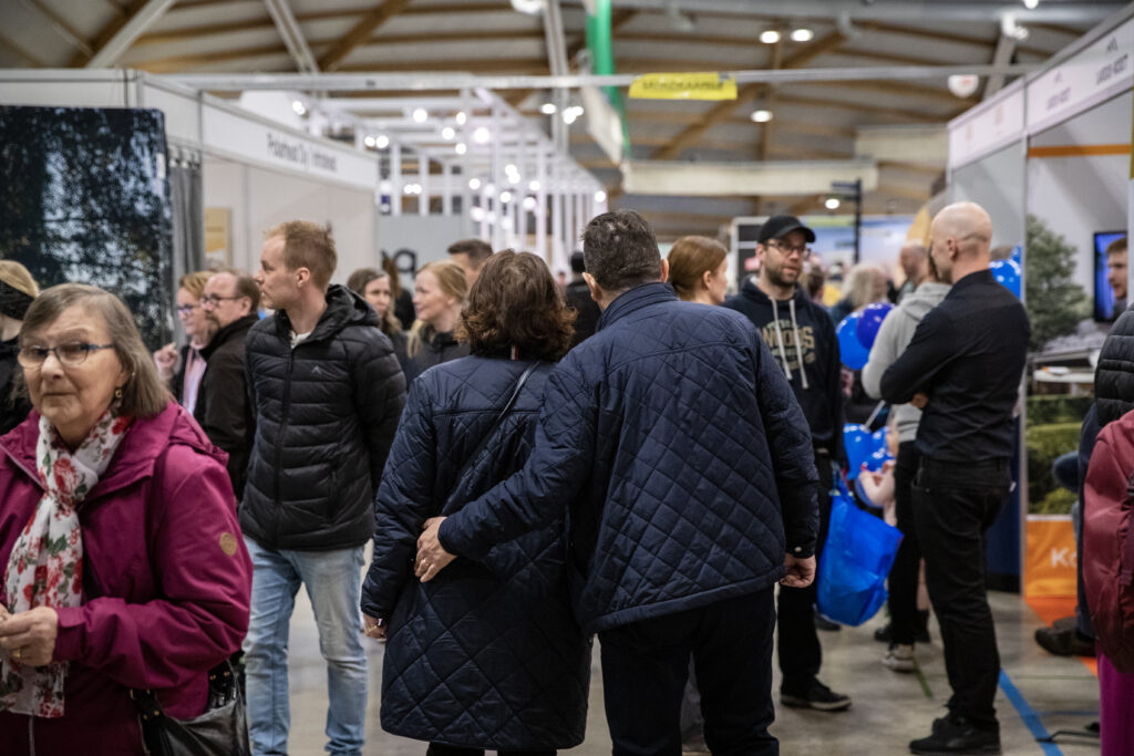 Vanhemoi pariskunta kävelee selin Rakentajamessujen väkijoukossa, mies pitää hellästi kättä naisen vyötäröllä